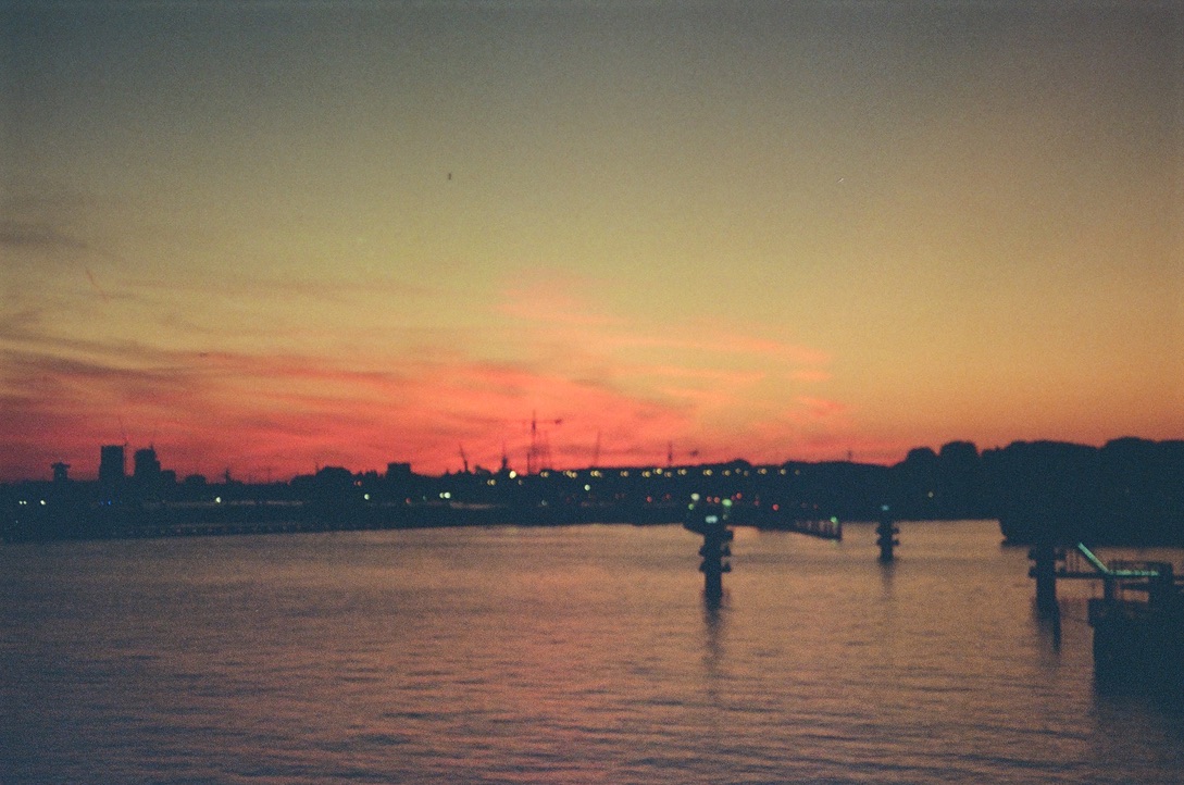 A grainy, blurry film photo of a glowing, red sunset above a body of water